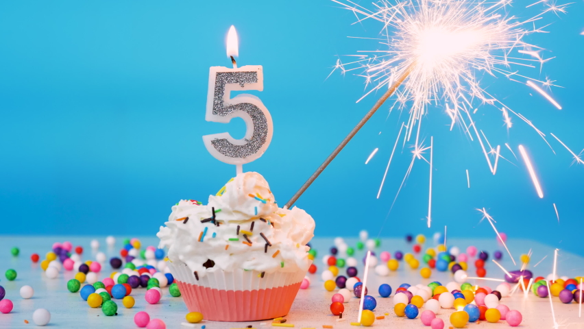 Happy birthday greetings to 5 year old child, birthday cupcake with candles and birthday decorations on blue background. Copy space Royalty-Free Stock Footage #1085211239