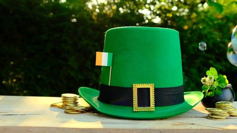 Saint Patrick festive.Soap bubbles,Green leprechaun hat,flag of Ireland,gold decorative coins on a wooden table in a sunny garden. 4k footage