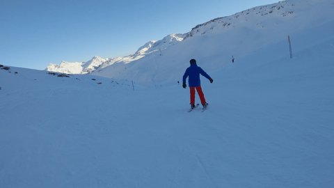 Follow shot, young man skiing downhill on ski slope in the Alps. Action camera filming skier descending technical piste 