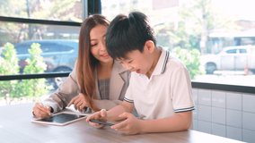 A boy playing game in smartphone and standing beside businesswoman in the coffee shop. Woman talking with kid. Happy and smile. Social media. Online technology. Education, learning and entertainment