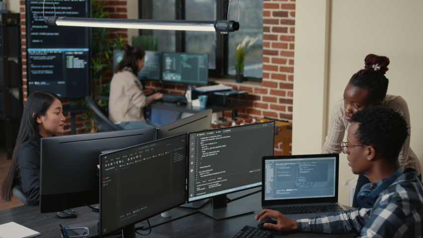 Mixed team of artificial intelligence cloud programers talking about programming in front of multiple screens compiling code. Programmers doing teamwork looking at machine learning algorithms. Royalty-Free Stock Footage #1085228894