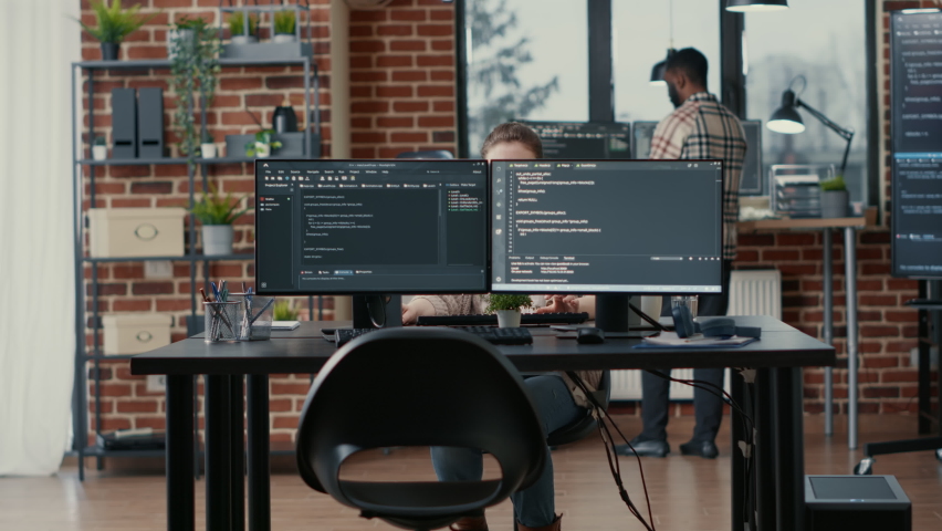 Programer coding on laptop sitting down at desk with computer screens parsing code in software agency. Software developer compiling algorithms with cloud programers working in the background. Royalty-Free Stock Footage #1085228975