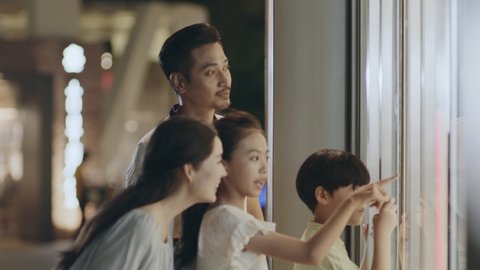 Asian family parents and kids standing and looking into shopping mall window