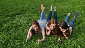 Three friends, young girls, having fun in park, laying on grass, slow motion.