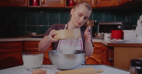 Woman Sifts flour through sieve in the Kitchen while baking croissants.