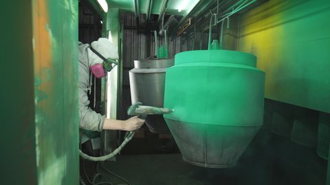 Industrial painting process in chamber. Painter spraying green paint on detail in special booth. Technician in safety wear work at industrial manufacture. Master paint parts in specialised workshop
