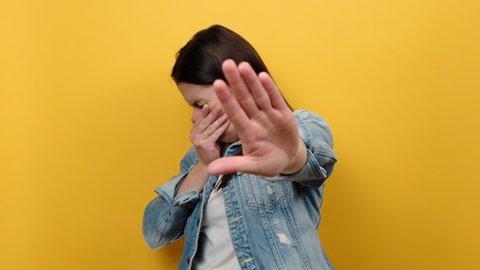 Portrait of young caucasian female grabbing nose with fingers, feeling unpleasant smell, shocked with disgusted fart, wearing denim jacket, posing isolated over yellow color background wall in studio