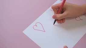 A boy draws a heart on a white sheet with a red felt-tip pen for a Valentine's day or mom's day card. Video