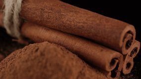 Cinnamon sticks and cinnamon powder isolated on black background, sliding shot. 4K UHD video