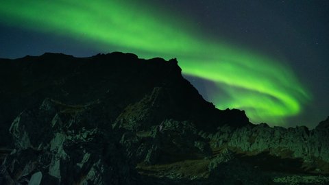 Mesmerizing dance of the northern lights in the starry sky above the dark silhouettes of the jagged rocks.