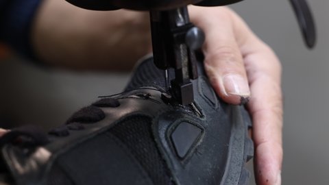 Shoe repairing. Sewing a shoe in shoe sewing machine for repairing. Senior man using machine in the workshop.