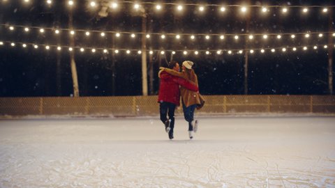 Romantic Winter Snowy Evening: Ice Skating Couple Having Fun, Step on Ice Rink and Start Dancing. Pair Skating. Young People Hold Halds. Boyfriend and Girlfriend in Love. Gradual Out of Focus Bokeh