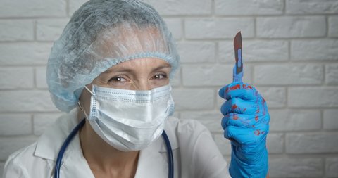 Dangerous scalpel. A crazy doctor hold a bloody scalpel in her hand in the room.