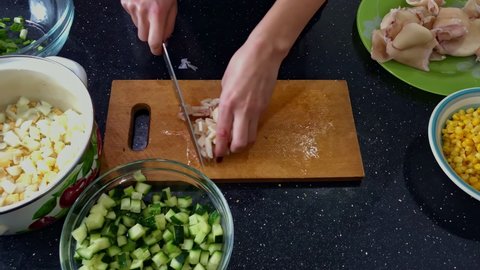 A housewife prepares squid meat by cutting it off with a knife on a kitchen board. Playing squid, cutting squid, cooking seafood. Delicious salad with seafood at home, eggs, onions, corn, recipes.