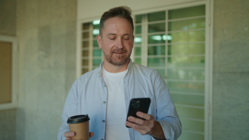 Young caucasian man using smartphone drinking coffee at street