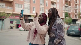 Two african american women smiling confident having video call at street