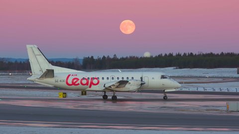 Oslo Airport Norway - December 16 2021: propeller airplane air leap taxiing passing full moon at very peri pantone colorful night
