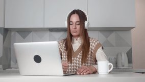 Happy caucasian young woman wear headset communicating by conference call speak looking at computer at home office, video chat job interview or distance language course class with online teacher