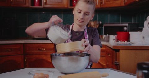 Woman Sifts flour through sieve in the Kitchen while baking croissants.