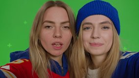 Two girls making selfie. Funny hipster females making self portrait . Young women in casual clothes having fun in front of green screen background. Chroma key