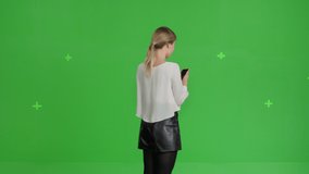 Girl reading text message on her mobile phone over green screen background, Young caucasian woman spins in place . Chroma Key 4k raw video footage