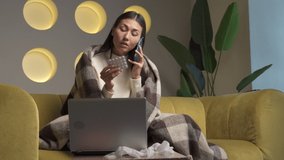 Sick Asian woman holds medicine, sits on the couch, makes a video call on the phone, consults with a doctor at home. The girl takes medications as prescribed by a doctor