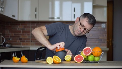 A man squeezes orange juice with citrus juicer. Close-up of hands, oranges, juicer, healthy lifestyle