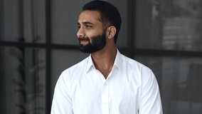 Close-up video portrait of a successful intelligent bearded Indian businessman, manager or IT specialist, ceo company, in modern office, wearing a white shirt, looking at camera with a friendly smile