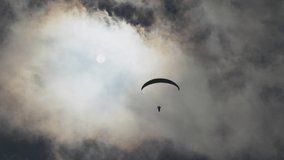 Paragliding adventure sport with parachute flying against bright sun hiding behind white cumulus clouds on blue sky on autumn day, 4K video