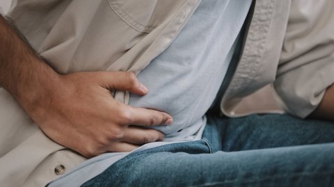 Close-up of male hands holding belly by side unrecognizable man feels bad digestive problems abdominal pain illness suffers from liver damage bending body in ache feeling unwell poisoning concept