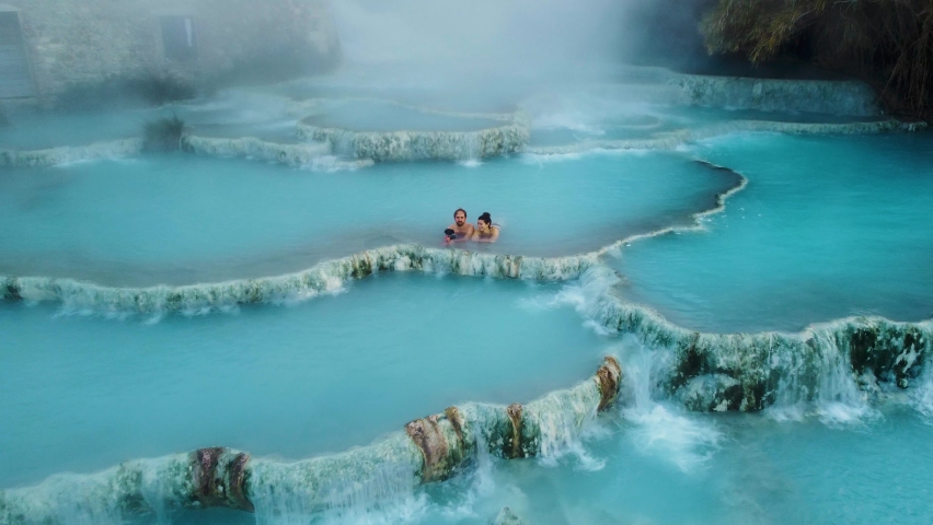 A young couple at the geothermal thermal hot springs bath and waterfall at Saturnia, Tuscany Italy close to Siena and Grosseto. Aerial drone at Cascate del Mulino, scenic and famous place in 4K UHD. Royalty-Free Stock Footage #1085267837