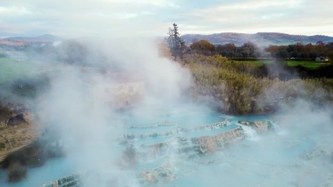 A young couple at the geothermal thermal hot springs bath and waterfall at Saturnia, Tuscany Italy close to Siena and Grosseto. Aerial drone at Cascate del Mulino, scenic and famous place in 4K UHD.