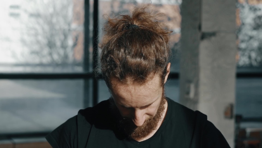 A handsome curly-haired guy with a beard looks at the camera. Happy confident smart young circus performer. Close up portrait of a serious man.