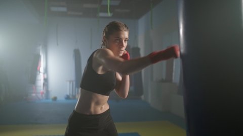 Woman fighter beats and kicking a punching bag, trains his punches, training day in the boxing gym, the female strikes fast.