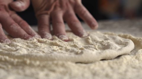 Hands crushing the dough. Chef preparing pizza dough. Dough and flour lying on the table against the background of a brick oven with fire. Pizzaiolo preparing dough with his hands. Slow motion