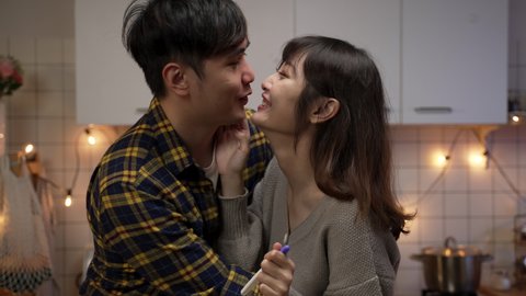 asian woman giving her husband valentine’s day surprise by showing positive pregnancy test result. married couple hugging and feeling excited about pregnancy