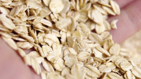 Dry oatmeal flakes in the palm of hand. A handful of uncooked whole rolled oats. Slow motion. Macro. Healthy organic cereal breakfast