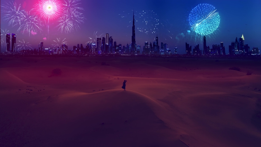 AERIAL. Young woman in traditional arabian dreess - abaya stands on the mounting at the desert and looks on the fantastic fireworks show at the modern Dubai city. Royalty-Free Stock Footage #1085279912