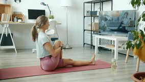 Beautiful young blonde is doing yoga at home watching tutorial on TV learning positions alone. Modern technology and healthy lifestyle concept.
