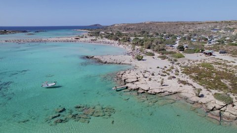 Aerial drone video of yacht anchored in volcanic exotic island bay with crystal clear turquoise sea water and shimmering pink sand. A boat is floating in the Elafonisi beach lagoon.