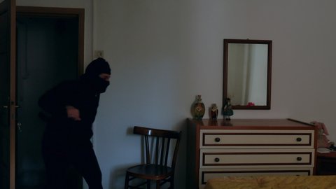 home burglary, a thief who enters an apartment through a closed window, opens the windows. thief dressed in black with balaclava.