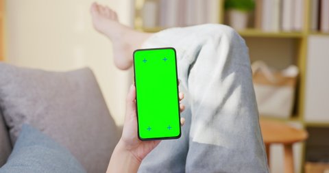 close up of asian woman with bare foot lying on couch is using green screen smart phone