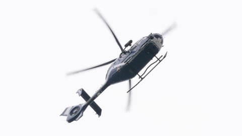 Police helicopter flying against a clear blue sky on a summer day - handheld video of surveillance by police forces