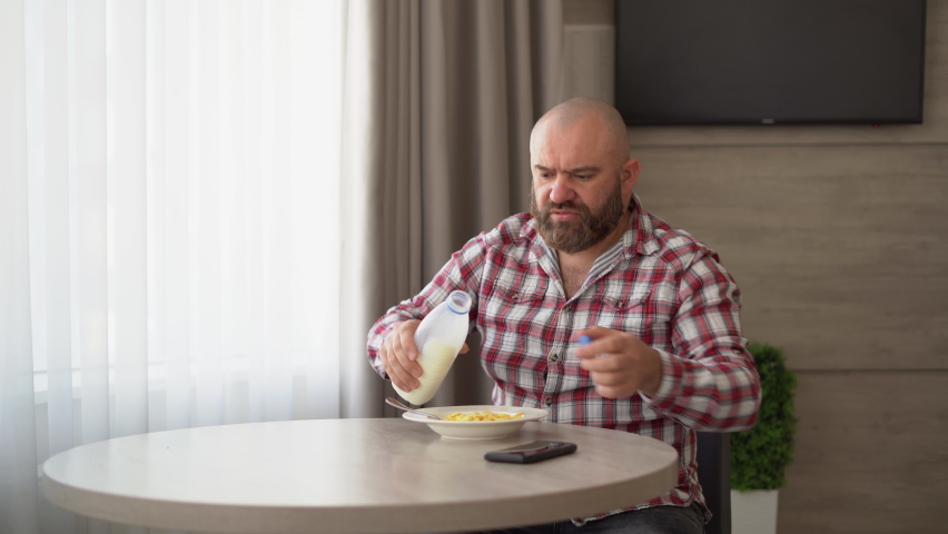man is having breakfast of cornflakes with milk, using a mobile phone, reads the news online.