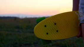 Close-up of a skateboard in the hands of a teenager who is standing at sunset. Life of teenagers and their subculture. Skateboarding.