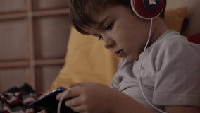 Child Happy Playing Games With Phone. Little Boy With Headphones Playing Video Game on Mobile Phone. Preschooler Plays Video Game On Smartphone. Eyesight Gambling Addiction