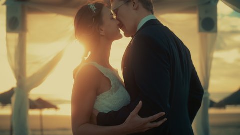 Close Up of a Bride and Groom During Outdoors Wedding Ceremony on an Ocean Beach at Sunset. Perfect Venue for a Couple to Marry, Exchange Rings, Kiss and Share Celebrations with Multiethnic Friends.