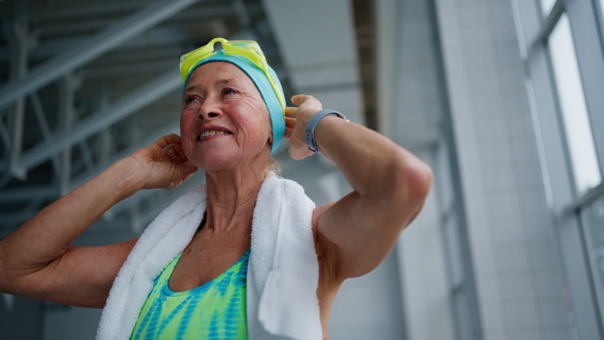 Low angle view of senior woman putting on goggles before swim in indoors swimming pool. Royalty-Free Stock Footage #1085290562