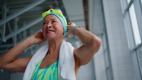 Low angle view of senior woman putting on goggles before swim in indoors swimming pool.