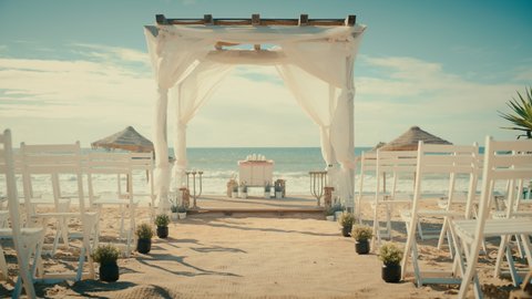 Empty Decorated Outdoors Wedding Venue with Chairs for Official Ceremony on a Beach Near the Sea or Ocean. Everything Prepared for Beautiful Romantic Marriage Celebrations. Zoom Out Shot.